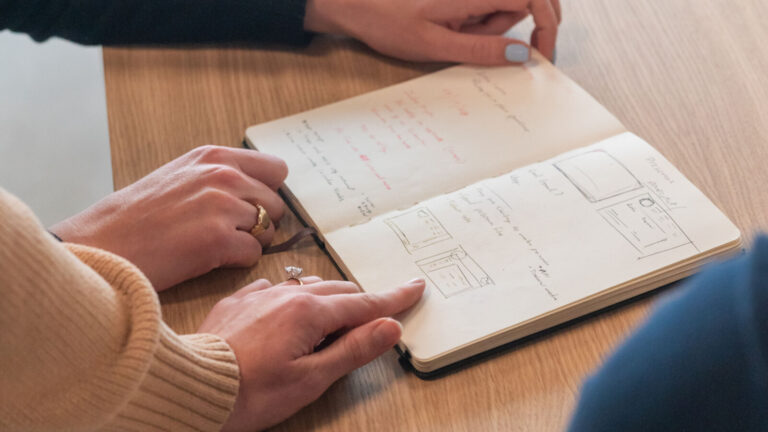 Fotos von Händen, die auf ein Notizbuch zeigen, das auf einem Holztisch liegt, mit Diagrammen, die die Funktionsweise von Index Marketplaces darstellen.