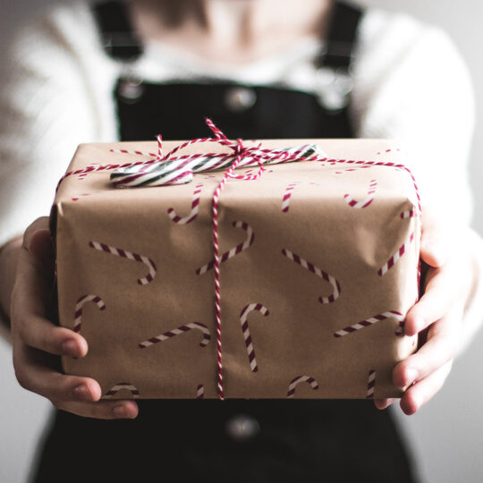 Photo d'une personne tenant un paquet cadeau enveloppé dans du papier avec un motif sucres d'orges sur fond blanc