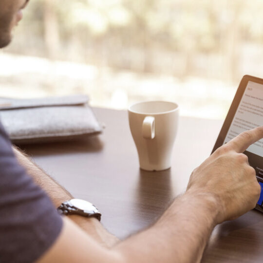 Foto di un uomo seduto a un tavolo che legge un articolo su un tablet per illustrare la possibilità di scegliere la tecnologia di pubblicità programmatica
