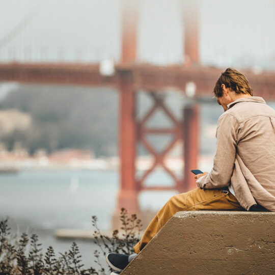 man looking at his cellphone with the golldengate bridge in the background