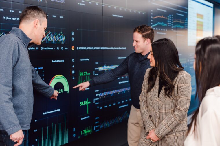 four-index-employees-gathered-around-data-filled-wall